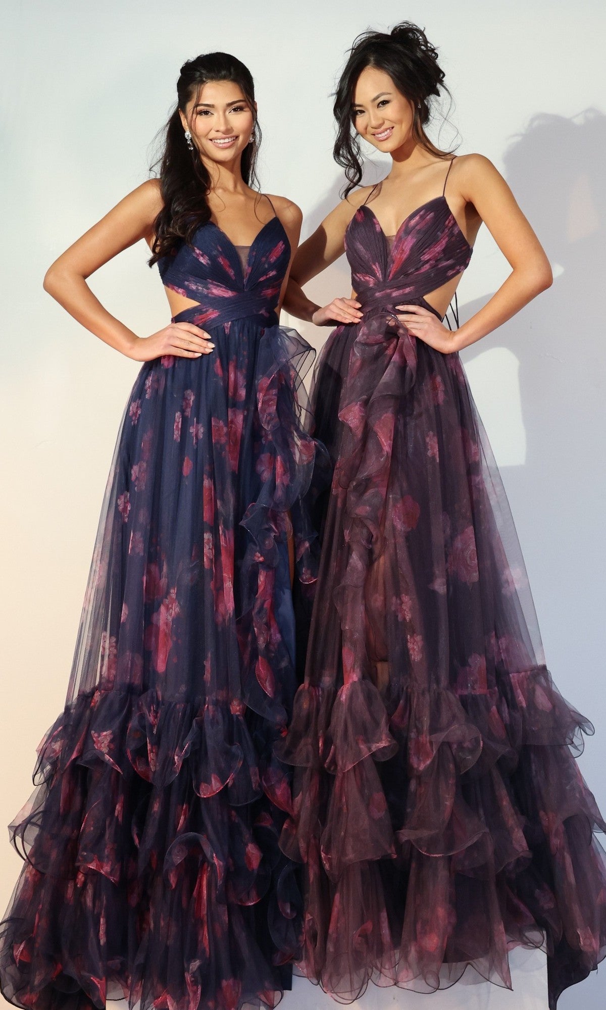 Two women stand side by side, each wearing a Jovani 45712 long prom dress featuring floor-length ruffles, delicate floral patterns, and spaghetti straps.